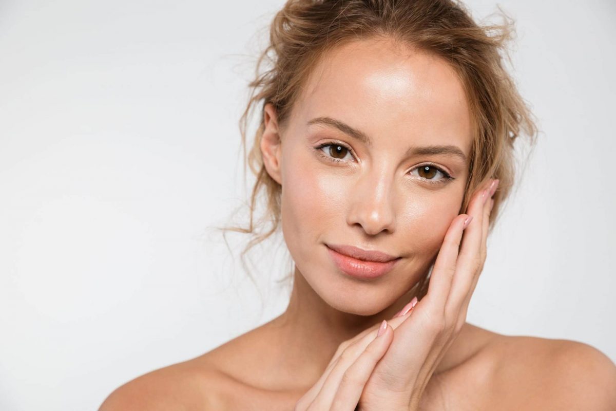 A woman smiling while touching her face.