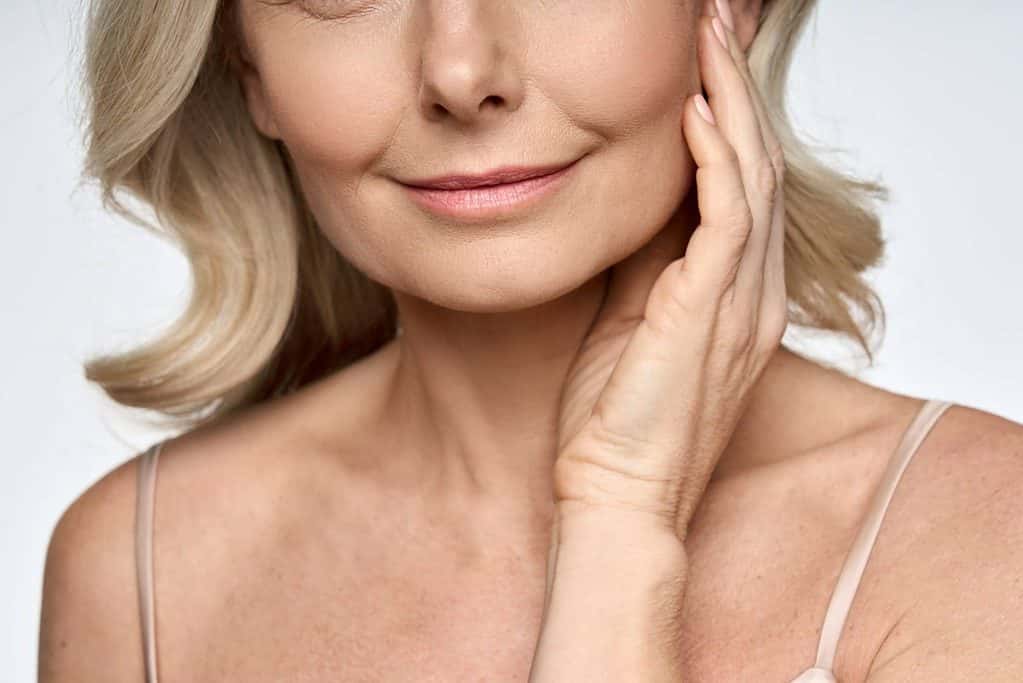 A woman in Scottsdale, Arizona smiling with one hand on her face after receiving Sculptra